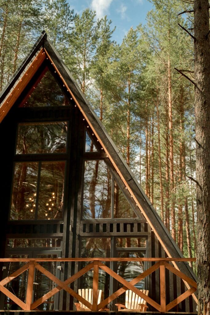 An a-frame cabin nestled in a remote forest with Christmas lights under the eaves decorated for a retreat.