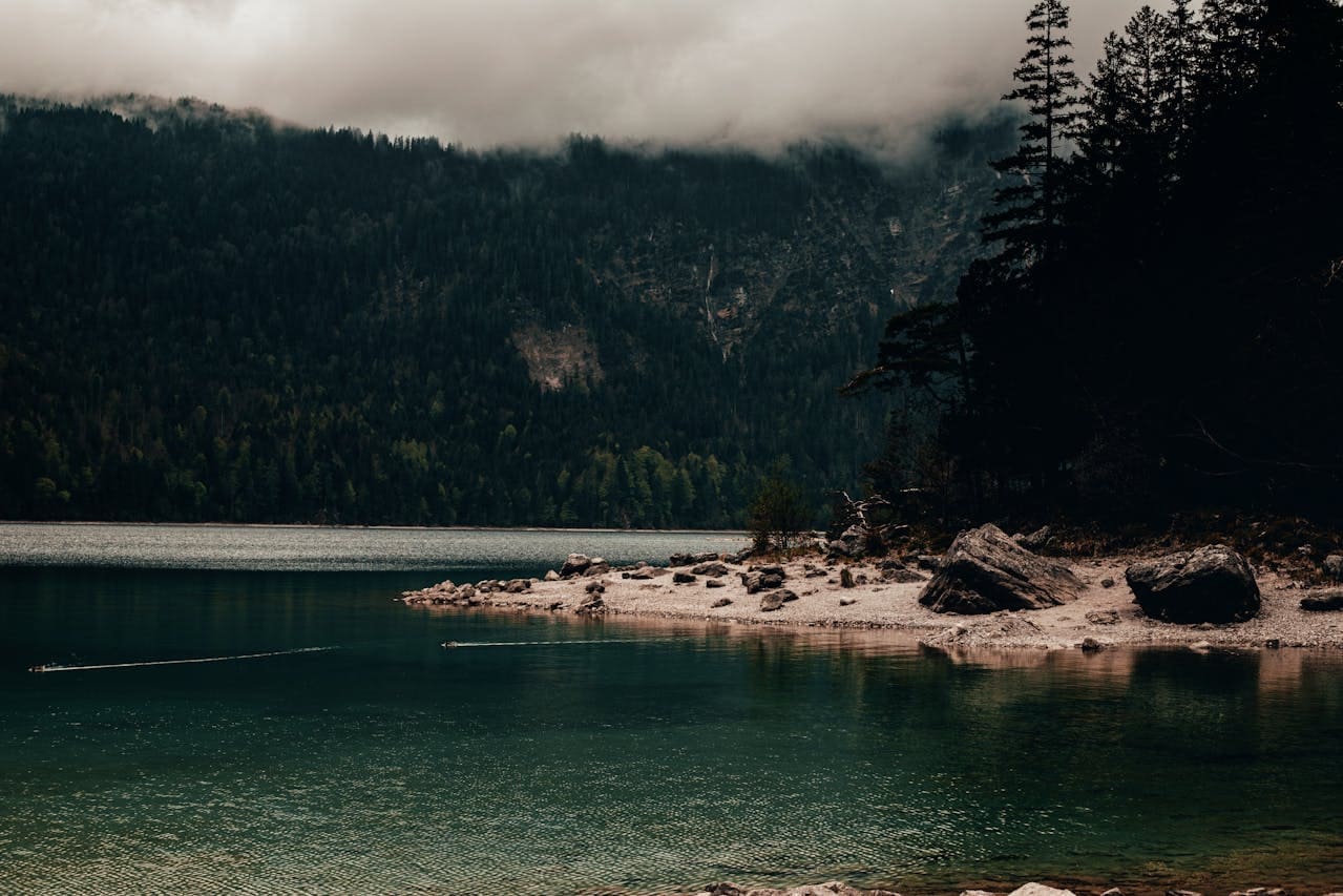 Moody mountain lake with rocky shoreline and foggy forested hills representing an adventure wellness guide online presence