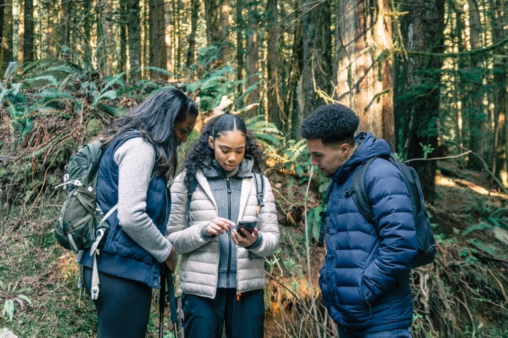 Three hikers in a forest looking at a phone together, searching for an outdoor wellness guide online