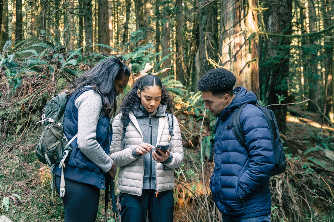 Three hikers in a forest looking at a phone together, searching for an outdoor wellness guide online
