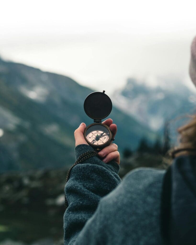 Person holding a compass against a cloudy mountain backdrop representing direction and clarity for an outdoor wellness business.